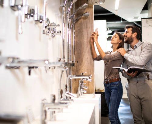 Husband and wife browsing for a shower head in a specialized store. Wife is taking a picture of a particular model on her smart phone.