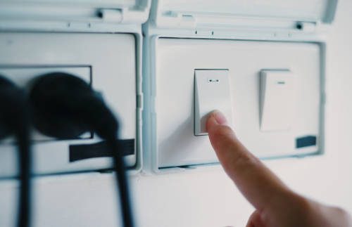 Selective focus of a woman's hand is pressing a switch to turn on a light in a living room at home.